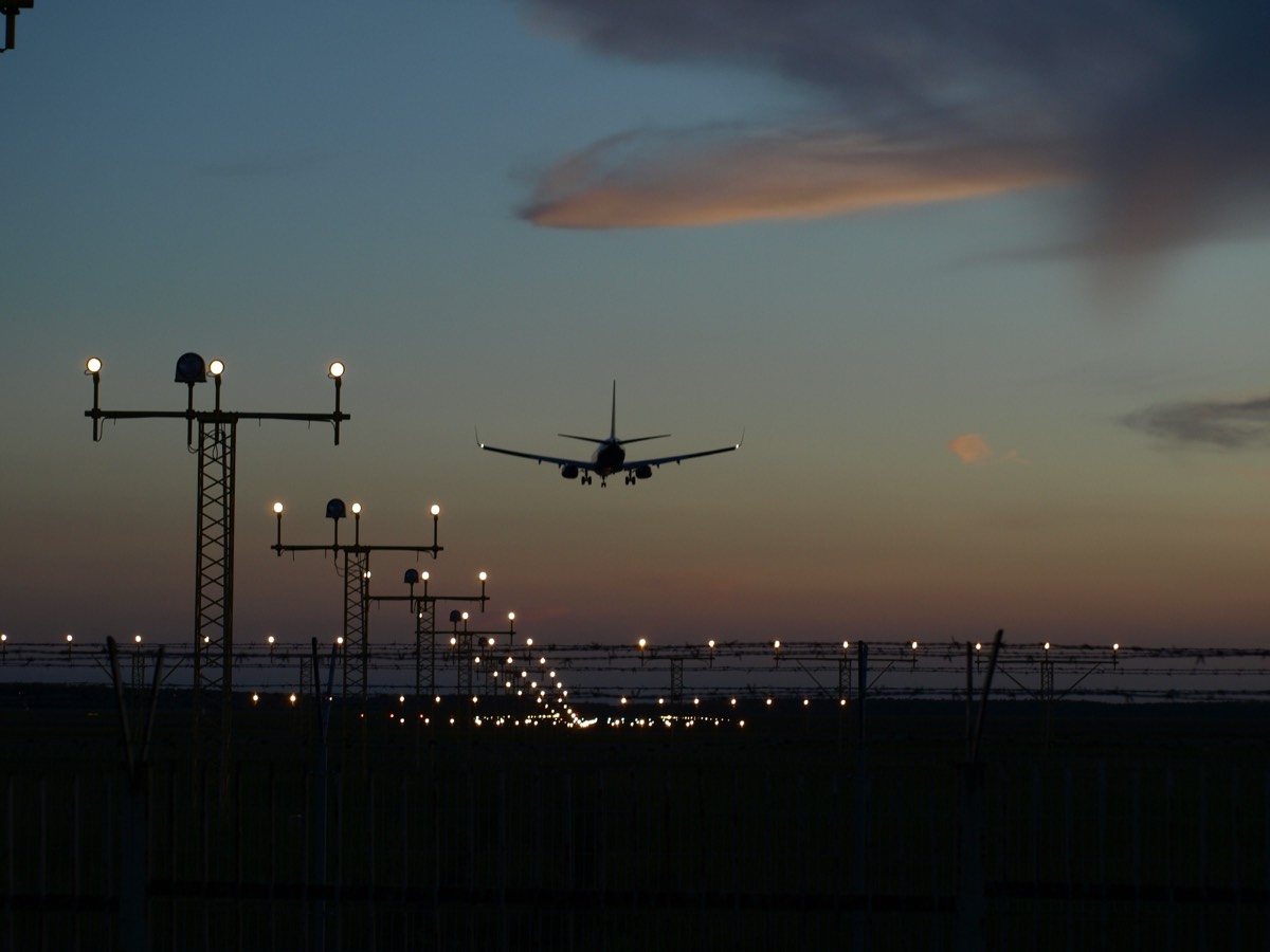 Approach lighting masts lit at dusk with an aircraft on final