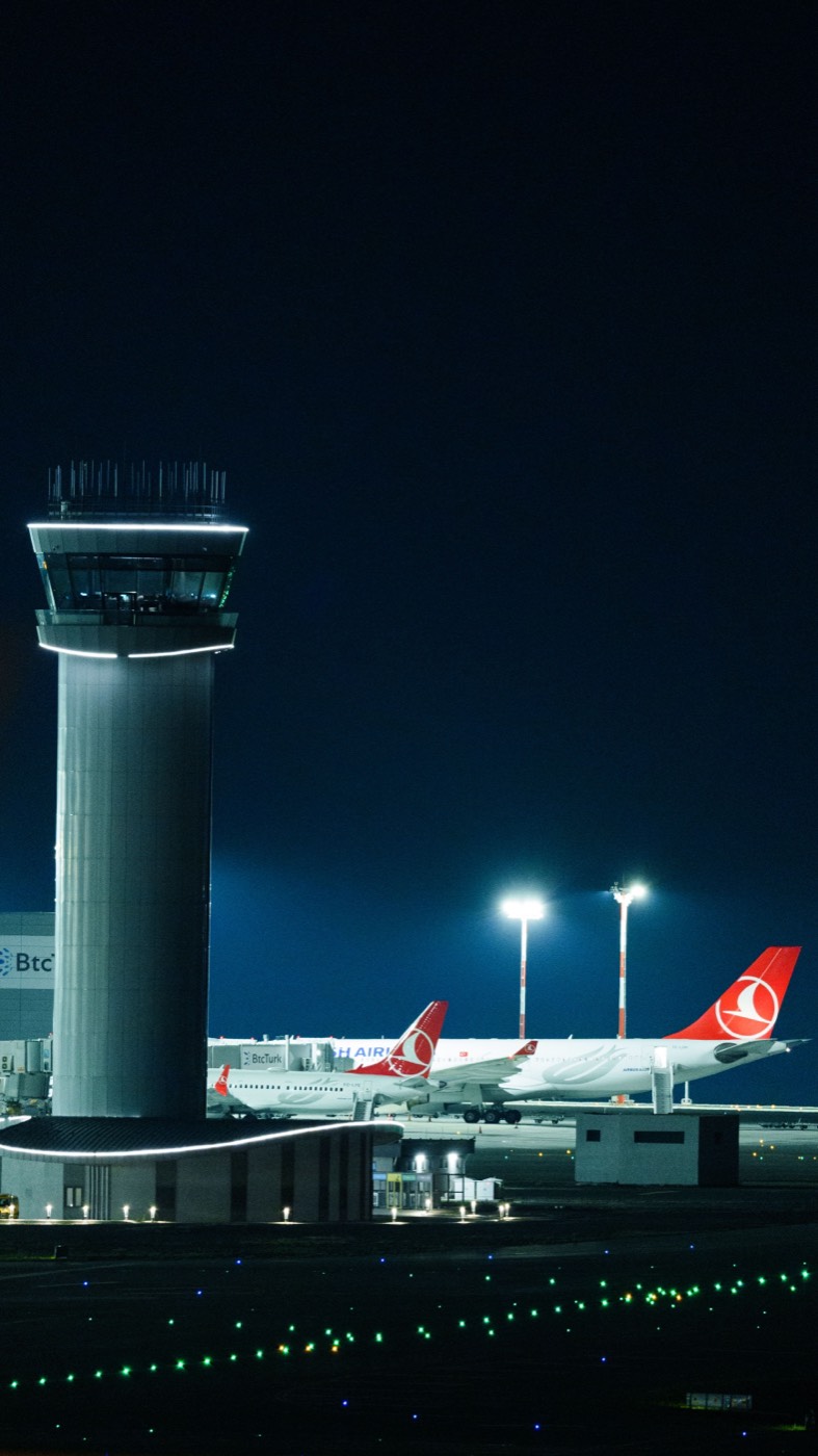 Airport control tower lit at night with aircraft on stand behind