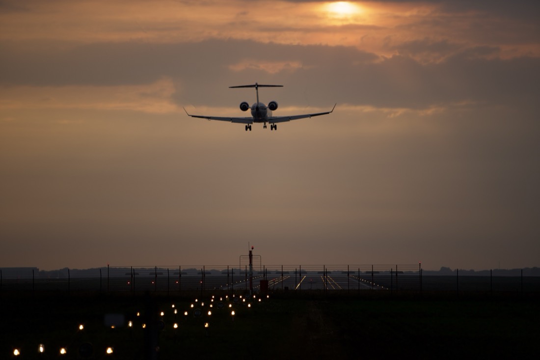 Aircraft on final approach over runway approach lighting at dawn