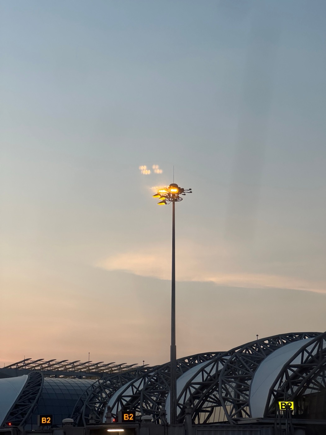High mast floodlight tower lit at dusk above a terminal roof